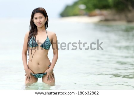 Beautiful sexy young Asian woman in a bikini at the seaside standing in the shallow water with wet hair