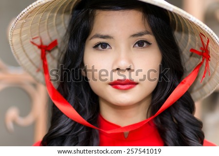 Pretty young Vietnamese woman in a red top with matching lipstick wearing straw hat, close up face portrait looking into the camera