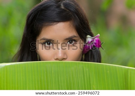 Portrait of a young Vietnamese woman peeking over the top of a banana tree leaf at the camera