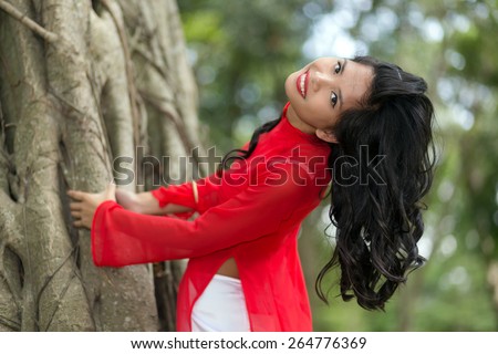 Charming Vietnamese woman bending over a large fig tree in a park, Vietnam