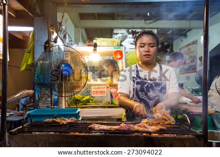 BANGKOK,THAILAND,FEBRUARY 16,2015: A woman is cooking chicken brochettes on barbecue in a small restaurant of the Sukhumvit Soi 38 in Bangkok,Thailand