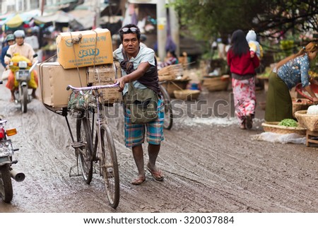 MANDALAY,MYANMAR,JANUARY 17, 2015 : A man is walking, using his bicycle to carry some boxes of food in the muddy street of the Zegyo outdoors market, in Mandalay, Myanmar (Burma).