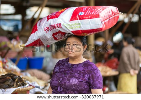 MANDALAY,MYANMAR,JANUARY 17, 2015: A woman is carrying a large monosodium glutamate bag on her head in the street of Mandalay, Myanmar (Burma).