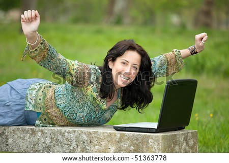 happy woman using laptop on park bench