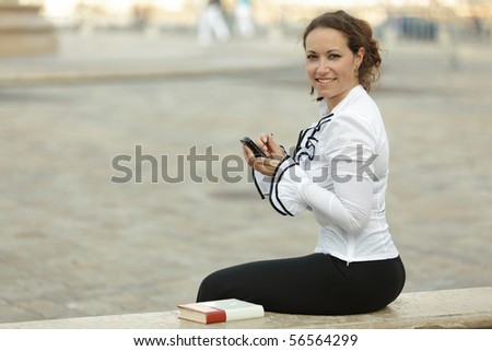 business woman sitting on stone bench using electronic organizer and looking at camera