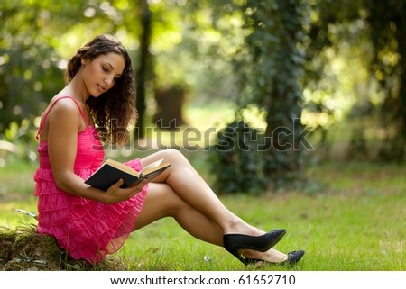 beautiful young woman in vivid pink dress reading book in nature