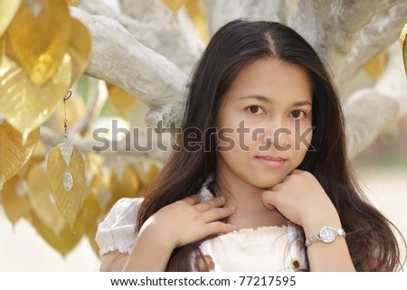 young asian woman posing near buddha lucky tree with golden leaves, Thailand.