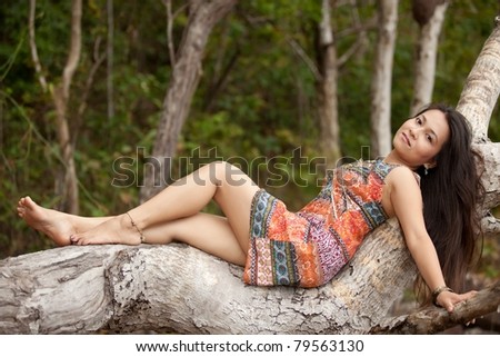 young asian woman relaxing on tropical tree trunk, thailand