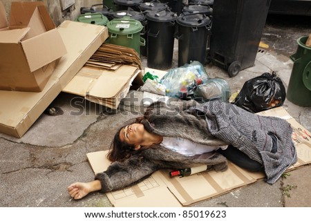 drunk tramp woman lying on cardboard in city trash area