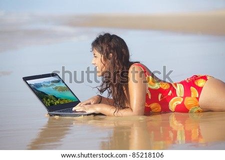 young woman surfing internet with laptop on wet sand
