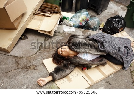 poor young drunk woman lying in trash in city street