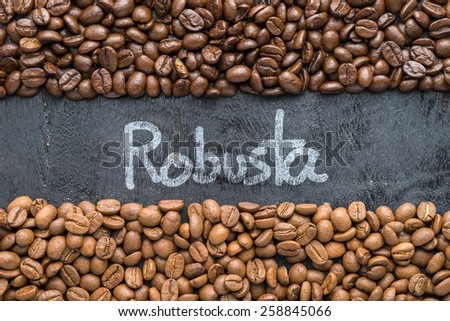 Coffee beans with Robusta hand writing on black wooden background with blank space.