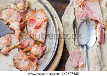 Cooked bacon slice being cooked in frying pan.