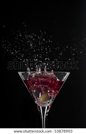 Cocktail splash with an olive on red martini with black background