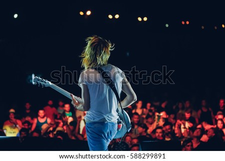 Guitarist on stage opposite the crowd at night open air. View from the stage
