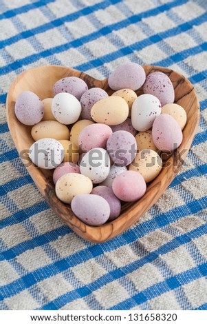 A wooden heart full of mini chocolate Easter eggs on a blue and white table cloth