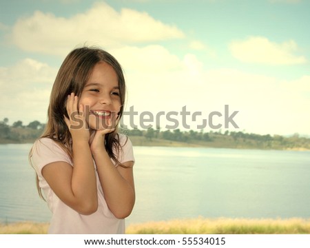 A young girl with an expression of joy, surprise and delight.  Standing on a shore of a lake.
