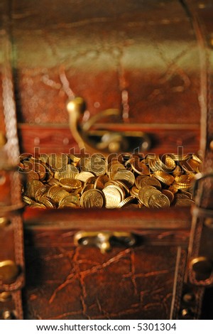 Reddish brown leather and wood treasure chest with gold colored coins (10 euro cent pieces) inside...Focus on the money inside