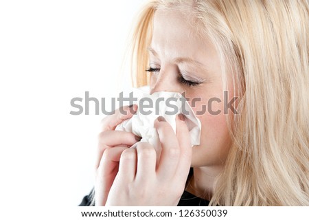 Closeup of blonde woman with cold sneezing into tissue