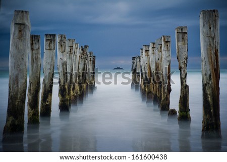 Wooden pier or jetty remains on a beach looking out to the pacific ocean, Dunedin, New Zealand