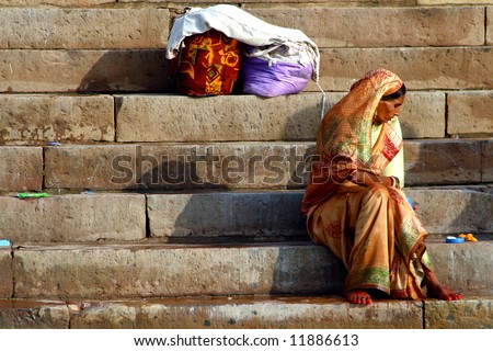 Woman in yellow sari seting on steps by rivers edge. Varanasi Uttar Pradesh India