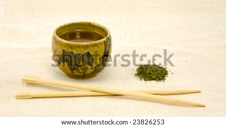 Closeup of Cup of Loose Green Tea with Chopsticks on Linen