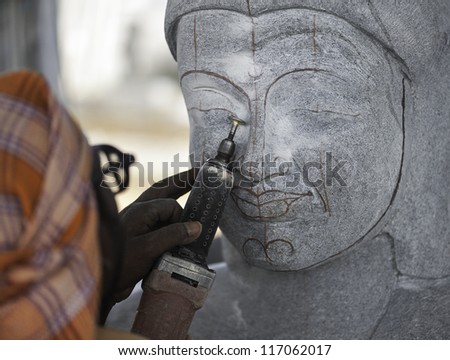 MAMALLAPURAM, INDIA - NOV 23,2011: Unidentified artisan uses modern tools to create a large granite sculpture of Lord Buddha on November 23, 2011 in Mamallapuram, Tamil Nadu, south India.