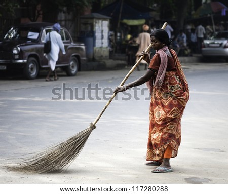 KOLKATA, INDIA - OCT 06, 2011: An unidentified woman in bright colorful sari sweeps along Park Street  with long broom during Durga Puja on October 06, 2011 in Kolkata, India.