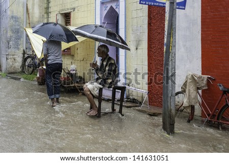 VARANASI, INDIA - AUGUST 11: a man sits patiently under an umbrella for heavy monsoon rain and flash flood to abate on August 11, 2011 in Varanasi, India.