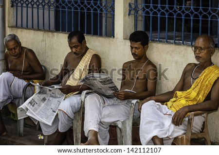 GUWAHATI, INDIA - SEPTEMBER 04: Hindu Brahmin temple priests take a break from religious conducting religious ceremonies and read newspapers on September 04, 2012 at Guwahati, Assam, India.