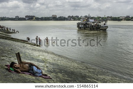 KOLKATA, INDIA - AUGUST 19: Life on the river Hoogly (Ganges) showing homeless man sleeping, people bathing, and public ferry plying the river on August 19, 2011, Kolkata, India.