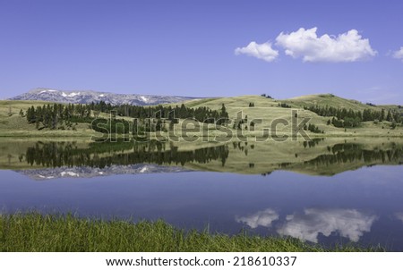 West Yellowstone, Wyoming, USA - Reflections of hills, trees, snow peaked mountains on a bring sunny day in Yellowstone National Park near West Yellowstone, Wyoming, USA.