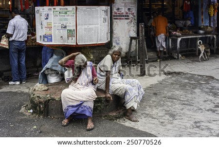KOLKATA, INDIA - AUGUST 17, 2011: Two poor women sit under free newspaper stand in front of shops  on August 17, 2011 in Kalighat area of Kolkata, India.