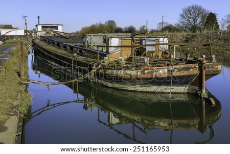 Beverley, Yorkshire, UK. A derelict river boat lays moored along the river Hull surrounded by reeds and overgrown vegetation near Beverley, Yorkshire, UK.