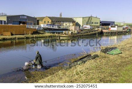 BEVERLEY, YORKSHIRE - FEBRUARY 09, 2015: Fishing on river Hull surrounded by derelict barges and current industry on a bright sunny morning on February 09, 2015 in Beverley, Yorkshire, UK.