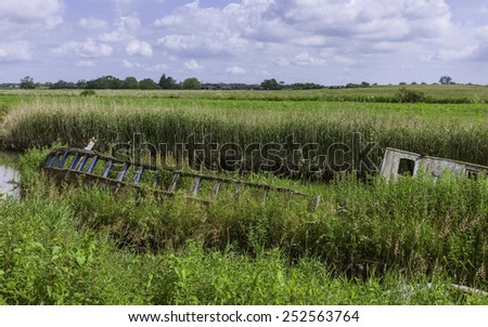 Beverley, Yorkshire, UK. A derelict river boat lays beached along the river Hull surrounded by reeds and overgrown vegetation near Beverley, Yorkshire, UK.