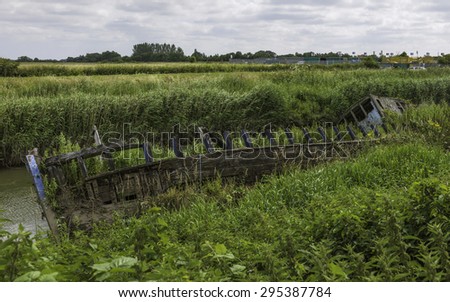 Beverley, Yorkshire, UK. Derelict wooden river boat half submerged in the waters of the river Hull surrounded by overgrown vegetation on a spring morning in Beverley, Yorkshire, UK.