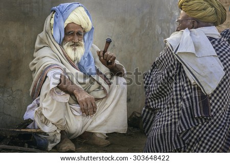 PUSHKAR, INDIA - OCTOBER 31, 2011: Two aging men dressed traditionally in turbans smoke a clay pipe at the end of the day\'s camel trading on October 31, 2011 in Pushkar, Rajasthan, India.