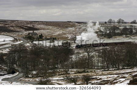 Goathland, Yorkshire, UK. Vintage steam train under full steam makes its way from Goathland to Pickering through the North York Moors covered in snow near Goathland, Yorkshire, UK.