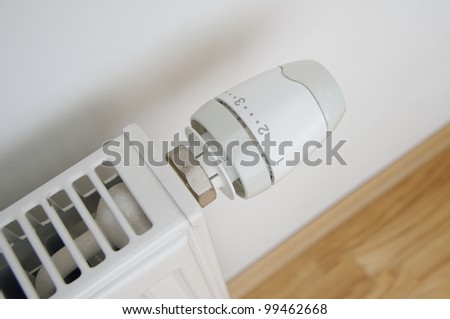 a close up of radiator regulator knob set to second level with wooden floor and wall visible
