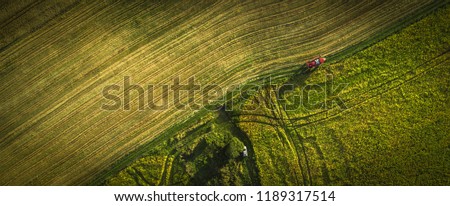 Aerial shot of tractor on the agricultural field sowing. Red tractors working on the agricultural field with sprayer.