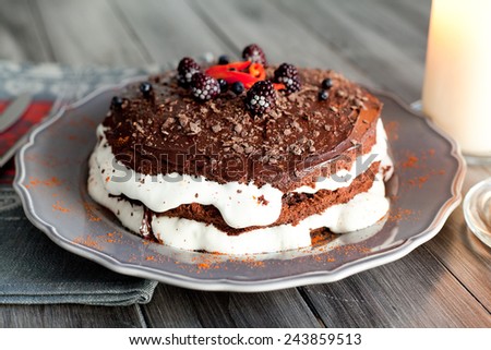 Homemade chocolate cake with white cream, decorated with a blackberry and pepper