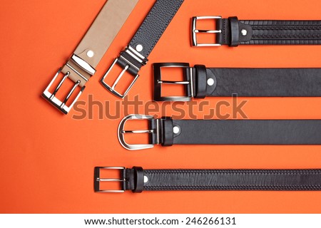 Studio close-up composition of six leather belts on orange background, shoot from the top