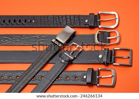 Studio close-up of six black leather belts on orange background