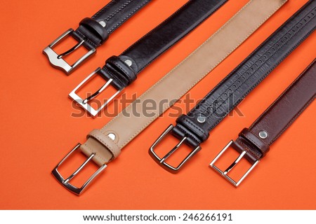 Studio close-up composition of five leather belts on orange background