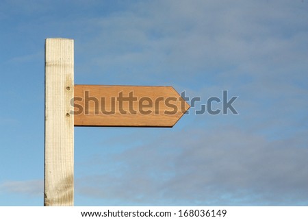 Wooden blank footpath sign pointing to the right against a blue sky.
