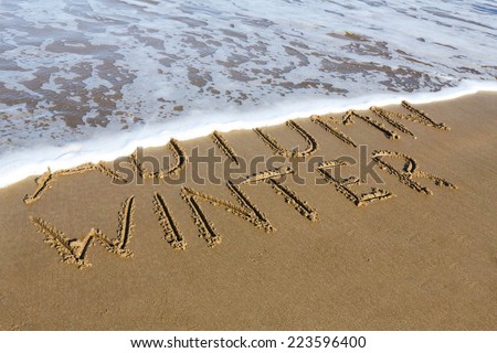Winter is coming concept - inscription Autumn and Winter written on a sandy beach, the wave is starting to cover the word Autumn.
