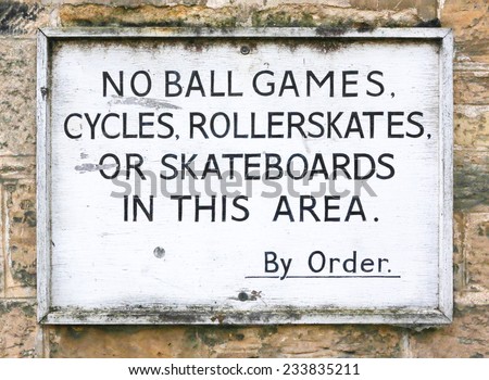 Old sign prohibiting ball games, cycling, roller skates and skateboarding on a stone wall background