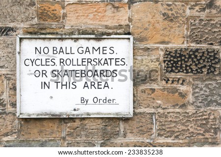 Old sign prohibiting ball games, cycling, roller skates and skateboarding on a stone wall background