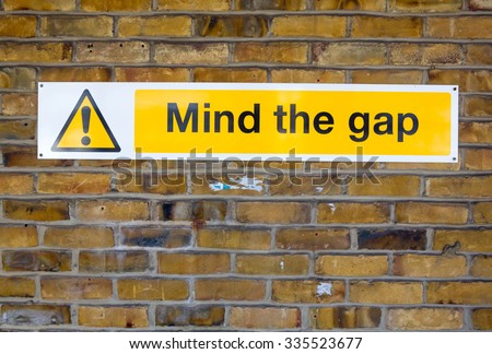 \'Mind the Gap\' yellow warning sign from the London Underground on a brick wall background